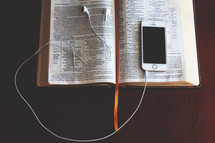 an iPhone and earbuds on a Bible 