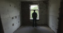 man looking out a window in an empty house 