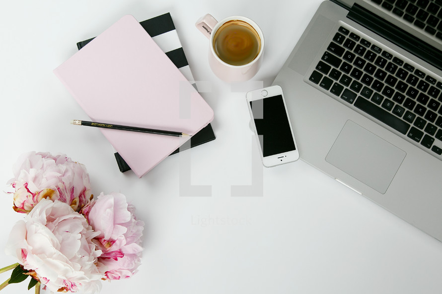 coffee, journals, planner, cellphone, pencil, laptop, and vase of flowers on a desk 