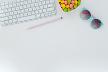 egg shaped candy in a heart shaped bowl, pencils, and computer keyboard, and, sunglasses on desk 