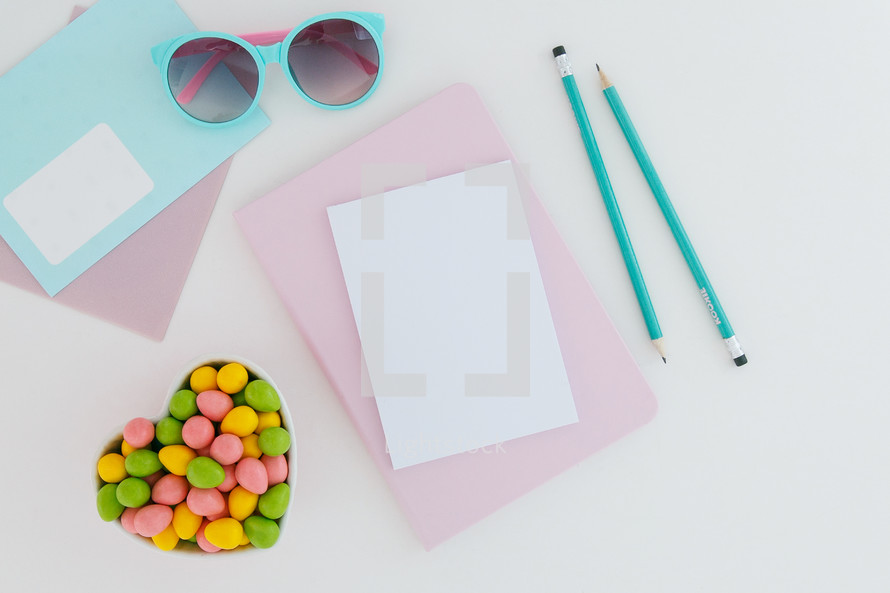 egg shaped candy in a heart shaped bowl, pencils, and stationary, chocolate bunny, and sunglasses on desk 