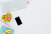 egg shaped candy in a heart shaped bowl, pencils, and computer keyboard, chocolate bunny, and sunglasses on desk 