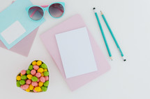 egg shaped candy in a heart shaped bowl, pencils, and stationary, chocolate bunny, and sunglasses on desk 