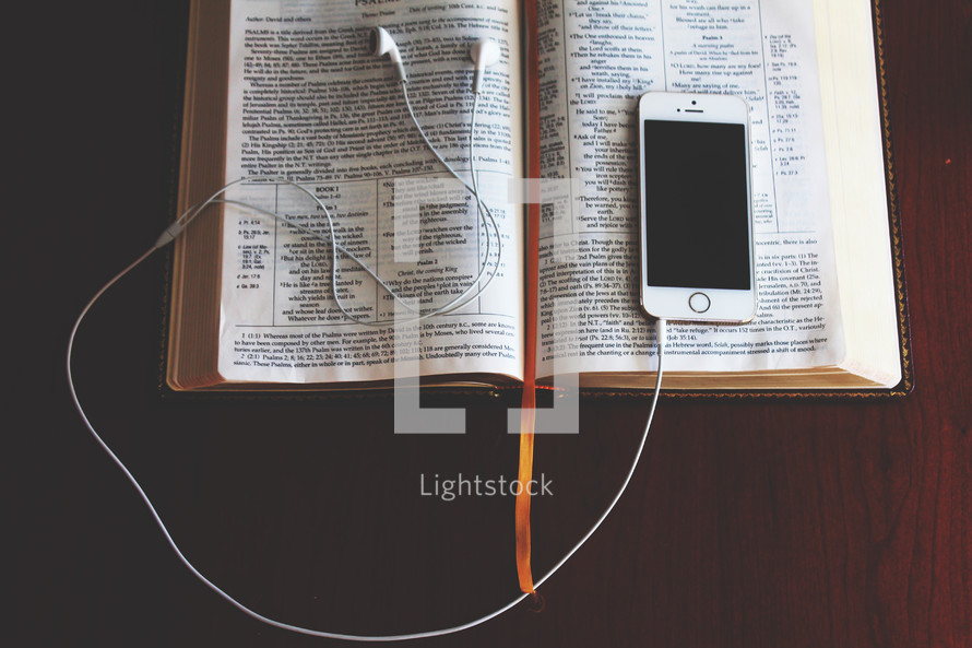 an iPhone and earbuds on a Bible 