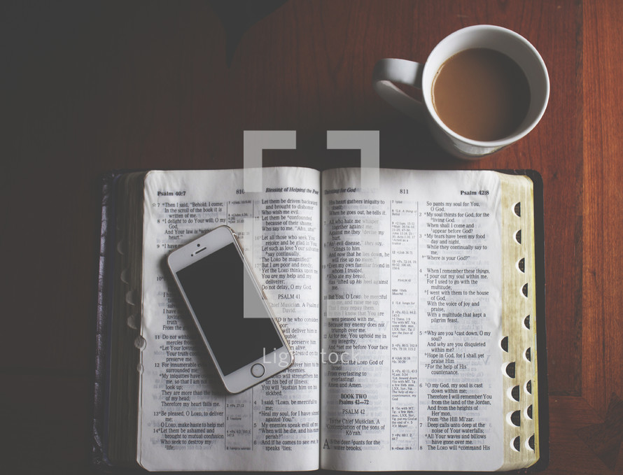 coffe mug and a cellphone on the pages of a Bible 