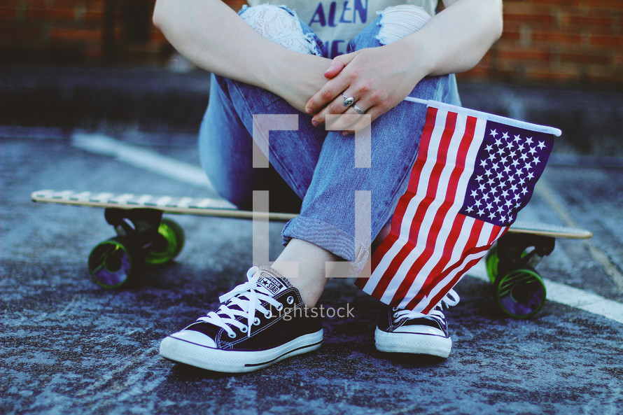 a teen sitting on a skateboard holding an American flag 